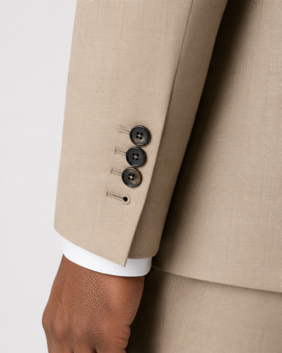 Close-up of a beige suit jacket sleeve with three dark buttons, a white dress shirt cuff, and part of a person's hand against a light gray background.