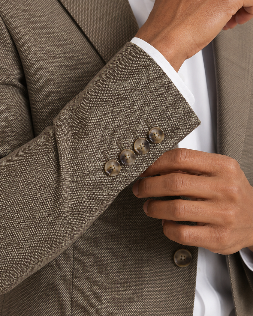 Close-up of a man wearing a brown textured blazer over a white dress shirt, adjusting his cuff with one hand and buttoning the jacket with the other.