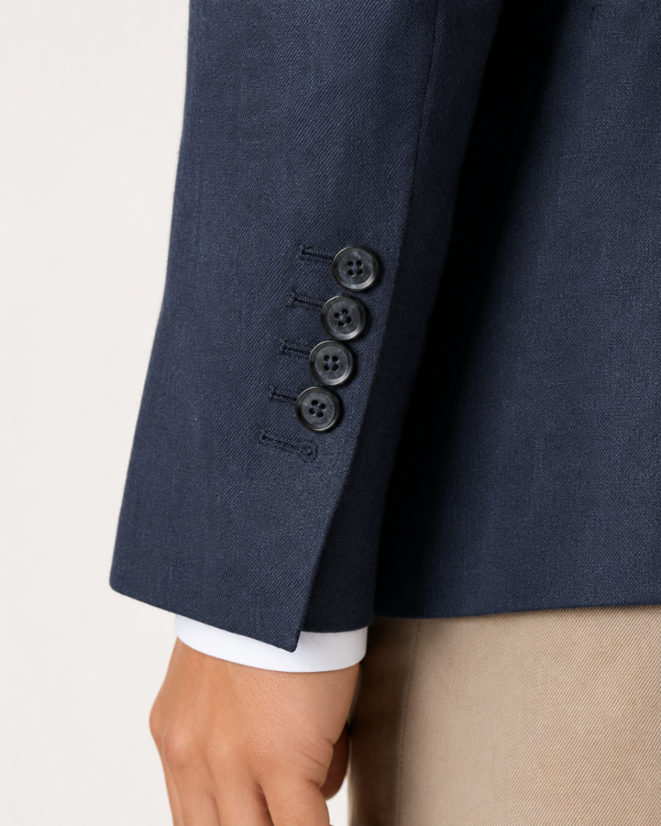 Close-up of a navy blue suit jacket sleeve with four dark buttons, worn over a white dress shirt cuff and paired with beige trousers.