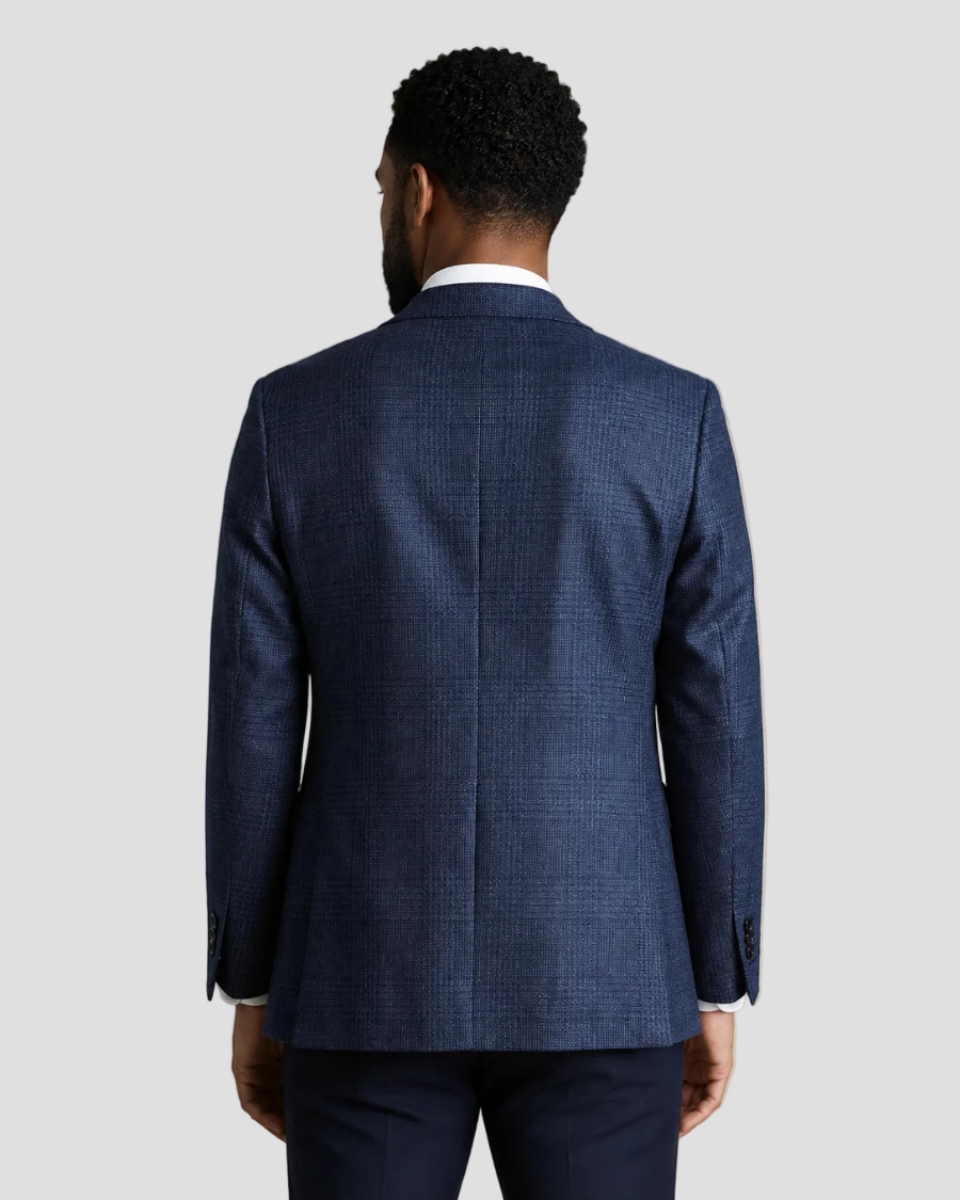 A man viewed from the back wearing a navy blue textured suit jacket and matching trousers, paired with a white collared shirt, against a solid beige background.