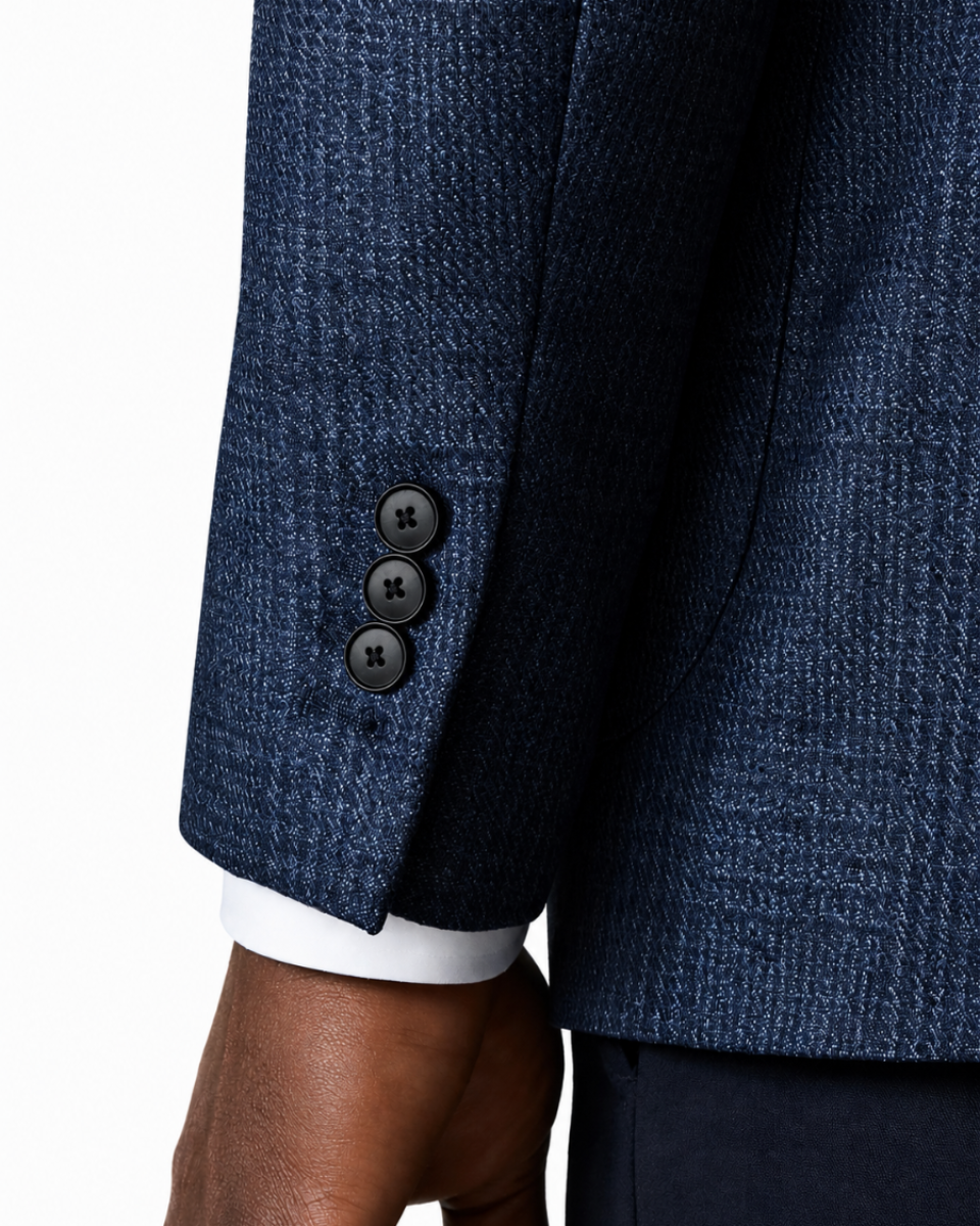 Close-up of a navy blue textured blazer sleeve with three dark buttons and a white dress shirt cuff, worn by a model.