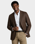 A man wearing a brown textured blazer over a white dress shirt and khaki trousers, standing against a solid beige studio background.