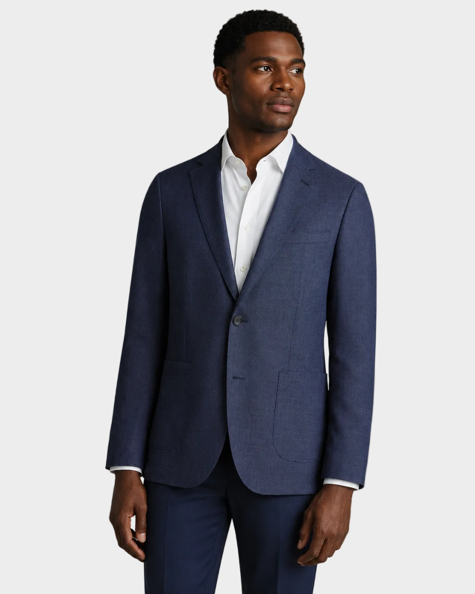 A man wearing a navy blue wool blazer with a white dress shirt, standing against a solid beige background.