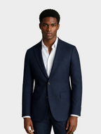 A man wearing a navy blue two-button suit jacket with a white dress shirt, standing against a solid beige background.