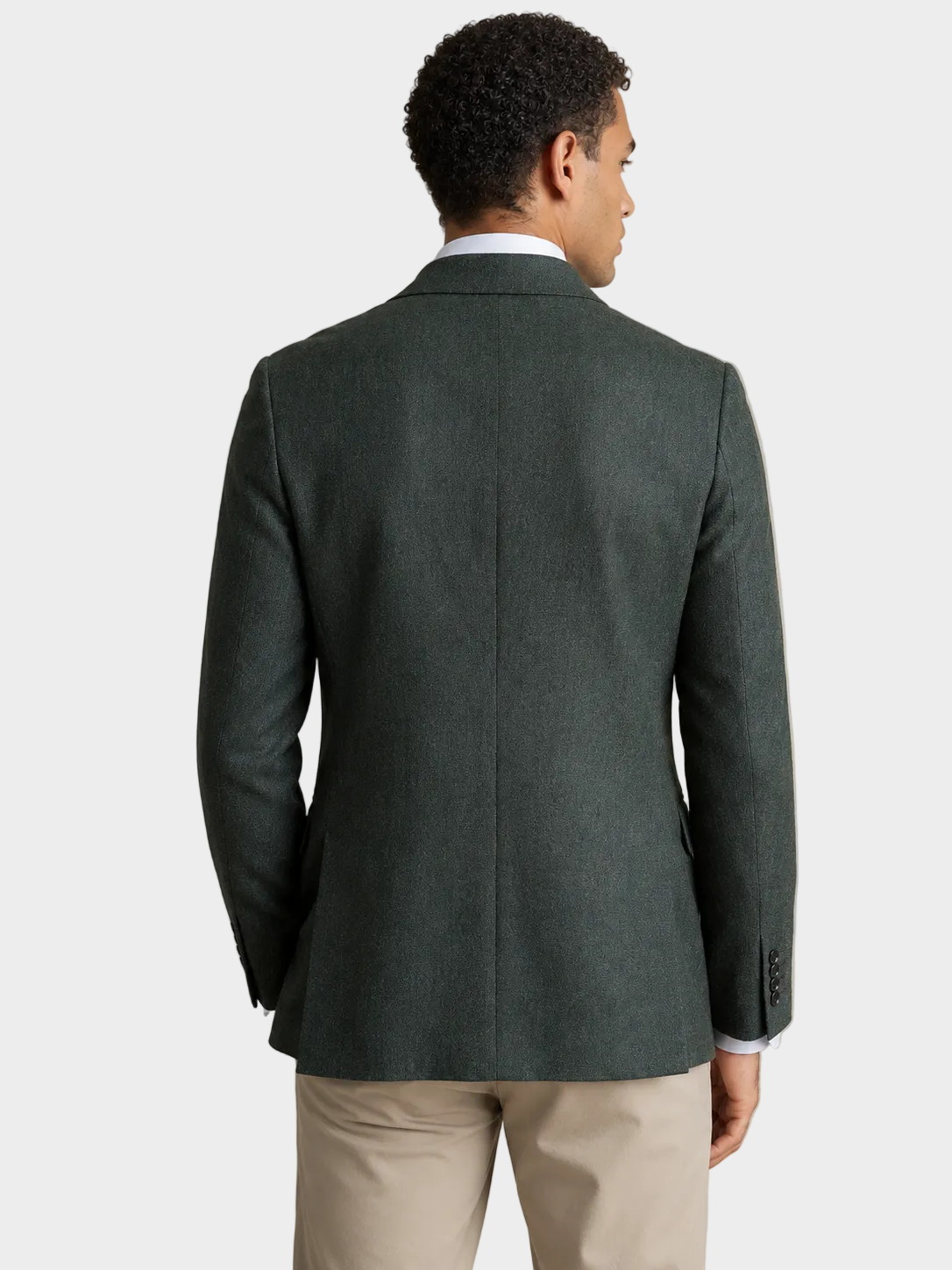 A man viewed from the back wearing a dark green textured sport coat over a white collared shirt and beige trousers, set against a plain beige studio background.