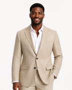 A man wearing a light beige linen suit with a white dress shirt, standing against a plain white studio background.