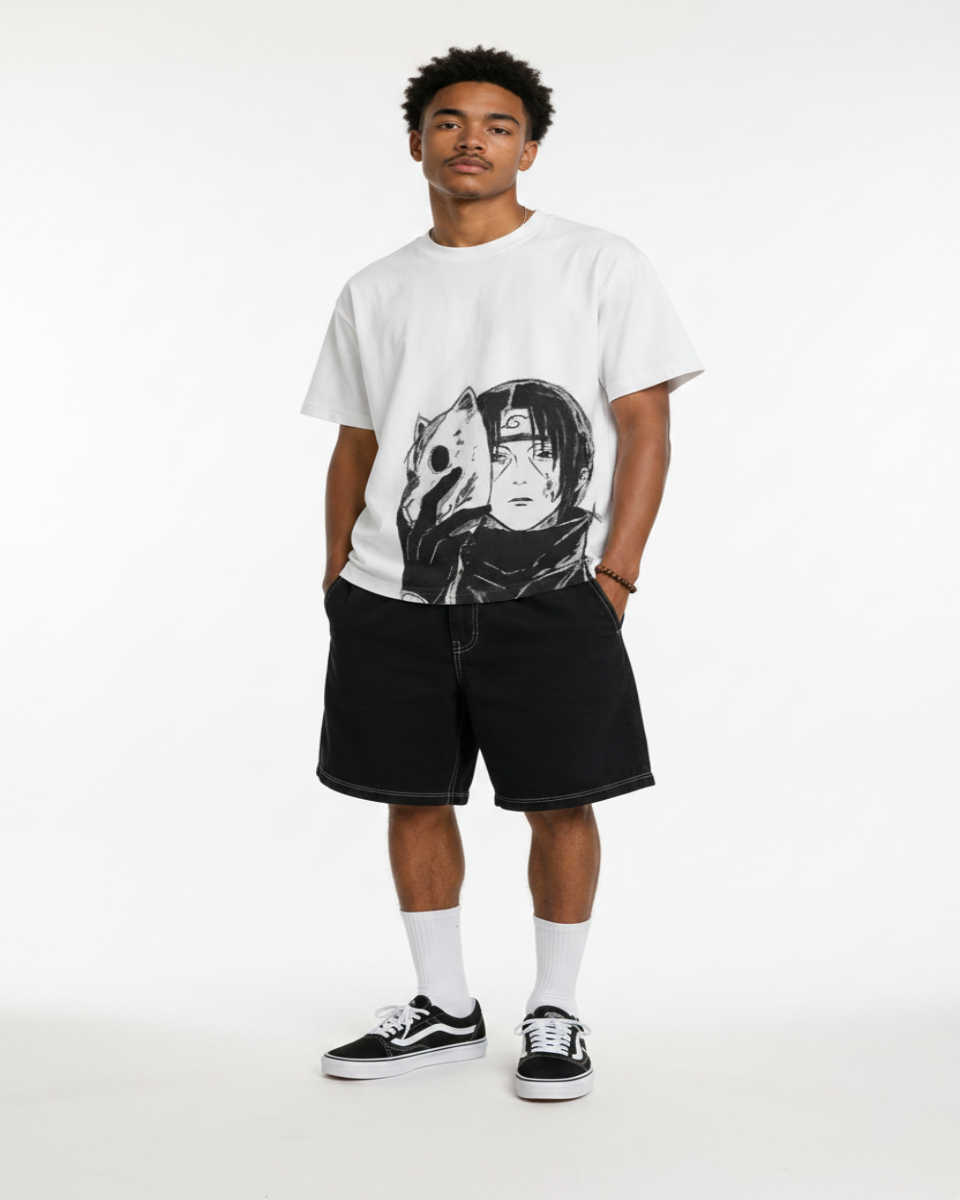 A man modeling a white graphic t-shirt with a black anime-style print, paired with black shorts, white socks, and black-and-white sneakers, standing against a textured gray wall.