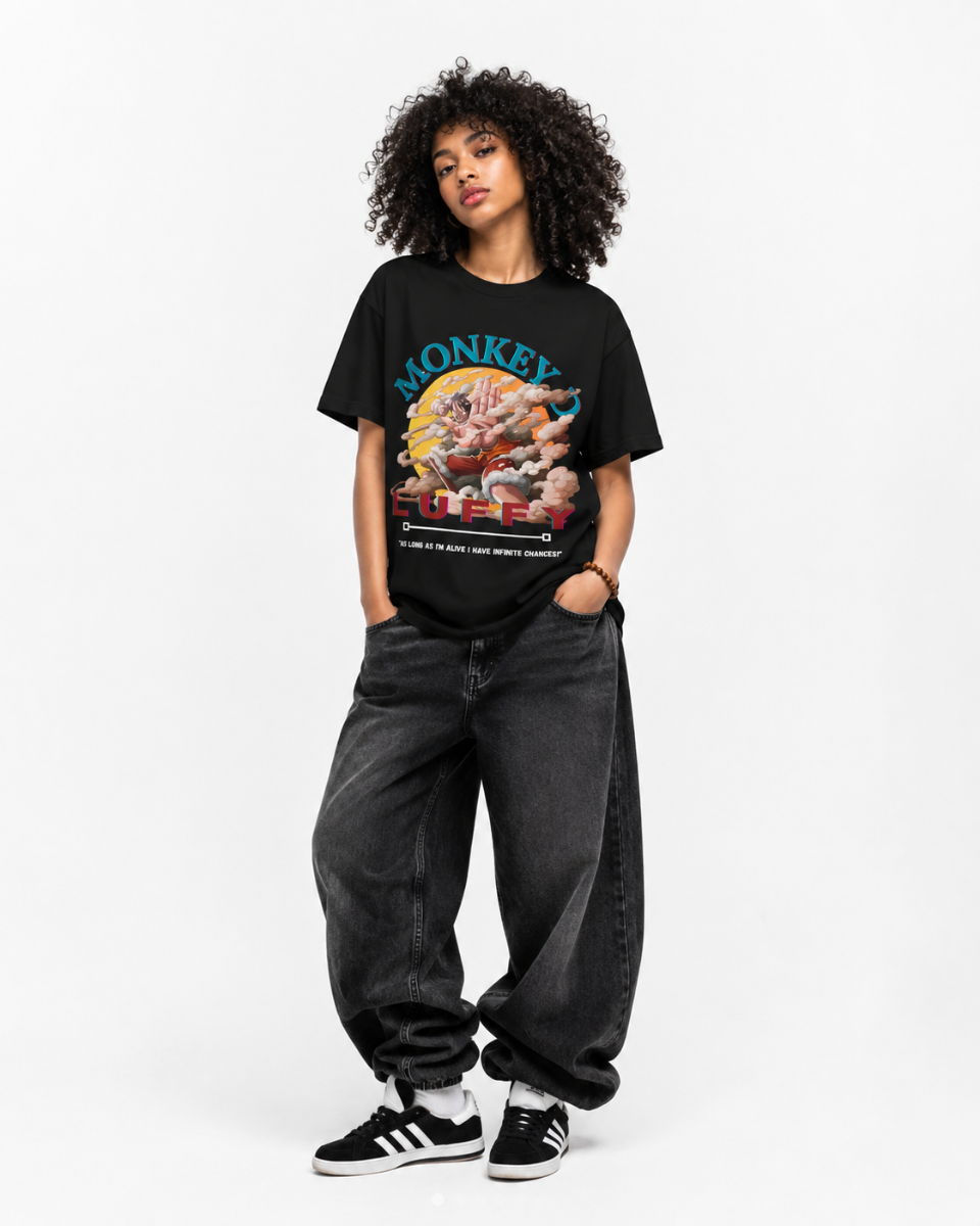 A model wearing a black graphic t-shirt with a colorful monkey print, paired with dark gray baggy jeans and black and white sneakers, standing against a plain white studio background.