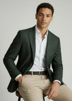 A man wearing a dark green textured blazer, a white dress shirt, and beige trousers, seated against a light gray studio background.