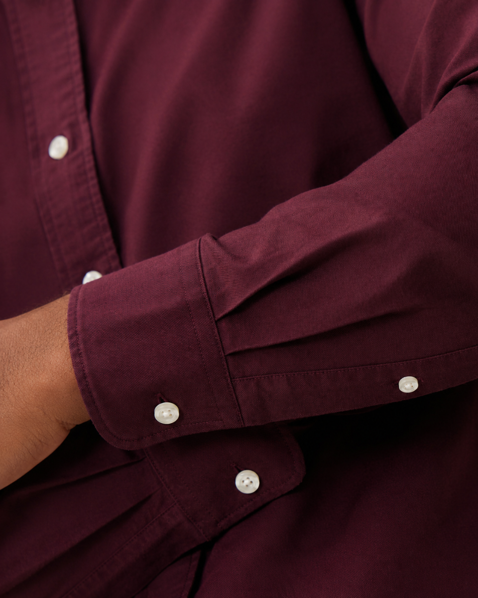 Close-up of a burgundy long-sleeve button-up shirt worn by a model, showing the fabric texture, cuff details, and white buttons.