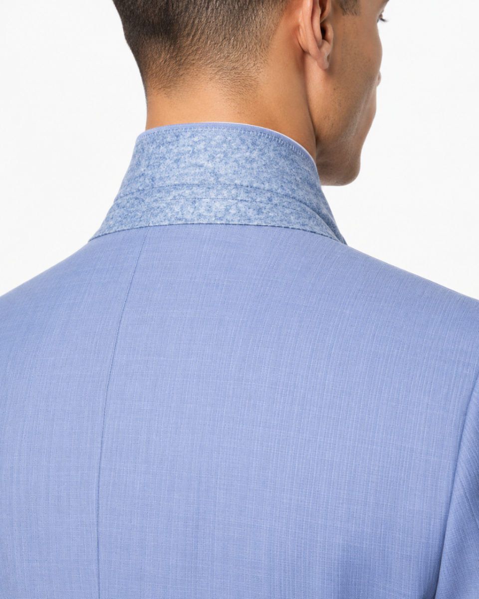 Close-up back view of a man wearing a light blue textured suit jacket with a patterned high collar, against a plain white background.