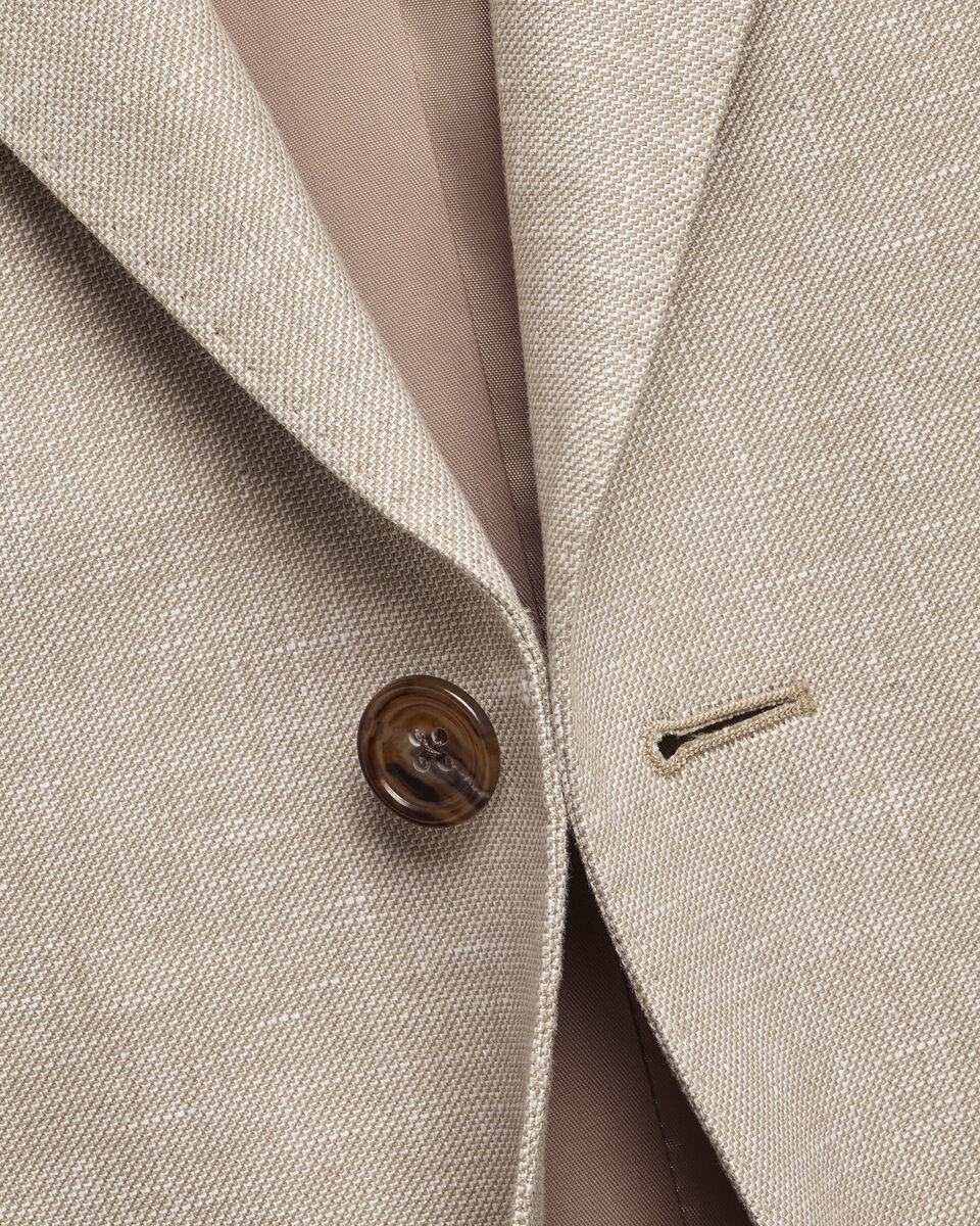 Close-up of a light beige textured suit jacket with a brown button and a subtle windowpane pattern, showing the lapel and inner lining.
