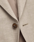 Close-up of a light beige textured suit jacket with a brown button and a subtle windowpane pattern, showing the lapel and inner lining.