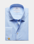 A folded light blue and white striped dress shirt with a pointed collar, button front, and a gold cufflink, shown on a light gray background. The inner neck label reads Martin & Co.
