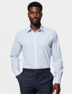 A man wearing a light blue and white micro-striped long-sleeve dress shirt with dark navy trousers, standing against a light gray studio background.
