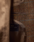 Close-up of a tweed jacket interior with a brown wool-like fabric panel, a dark navy brand label reading Es & Curtis, and a soft tan suede or suede-like flap.