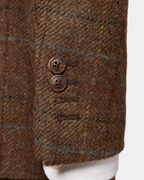 Close-up of a brown tweed blazer sleeve with a two-button cuff, showing the fabric texture and a white dress shirt cuff underneath.