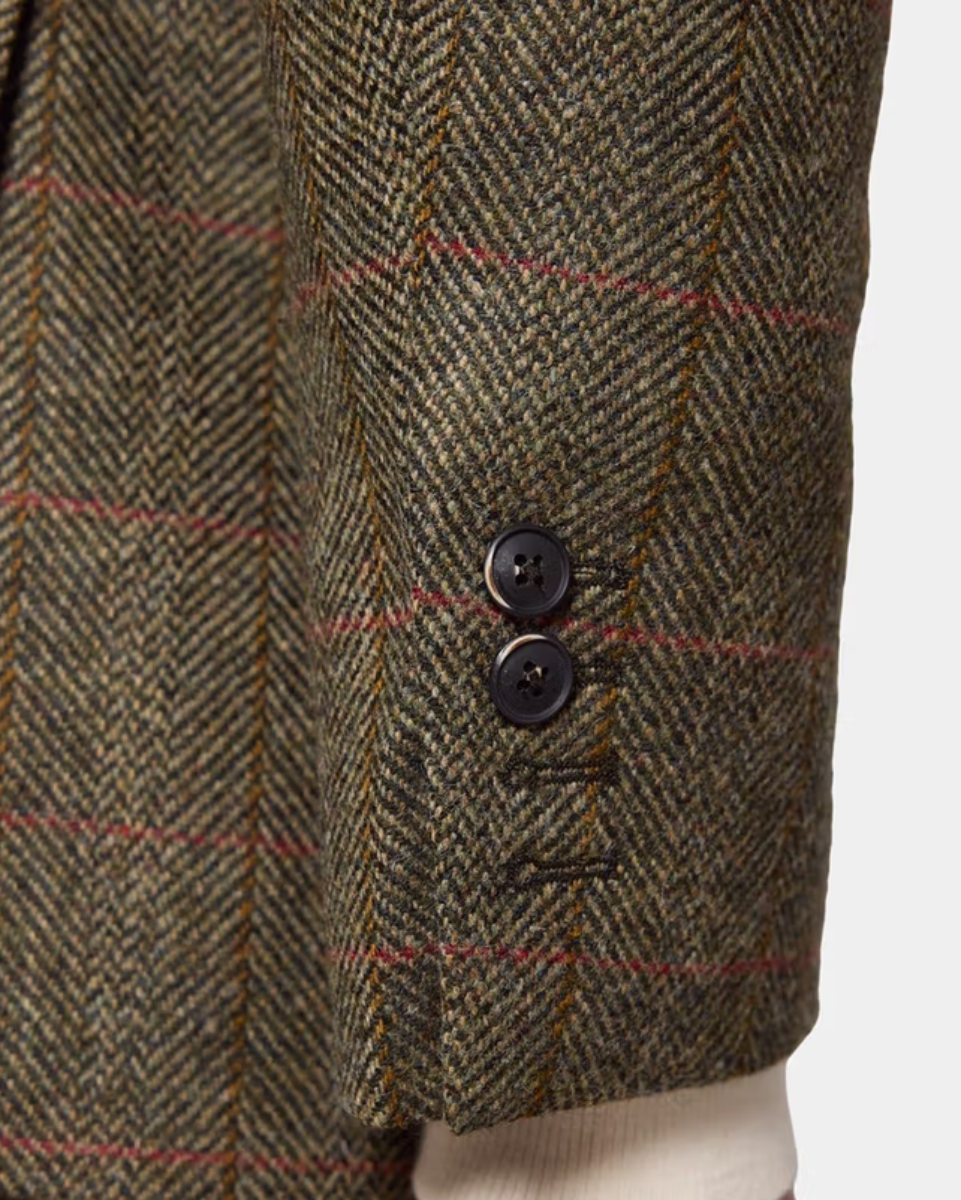 Close-up of a herringbone tweed jacket sleeve showing the fabric texture, a subtle red windowpane check, and two dark buttons on a light gray background.
