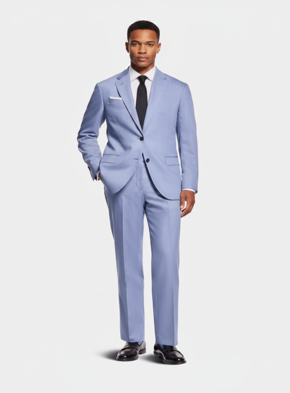 A man modeling a light blue three-piece suit with a white dress shirt, black tie, and black dress shoes against a light gray studio background.