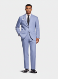 A man modeling a light blue three-piece suit with a white dress shirt, black tie, and black dress shoes against a light gray studio background.