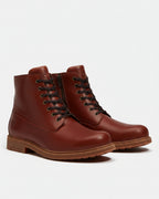 A pair of men's leather lace-up ankle boots in a rich reddish-brown color, featuring black laces, a side zipper, and a rugged brown sole, shown against a light gray background.