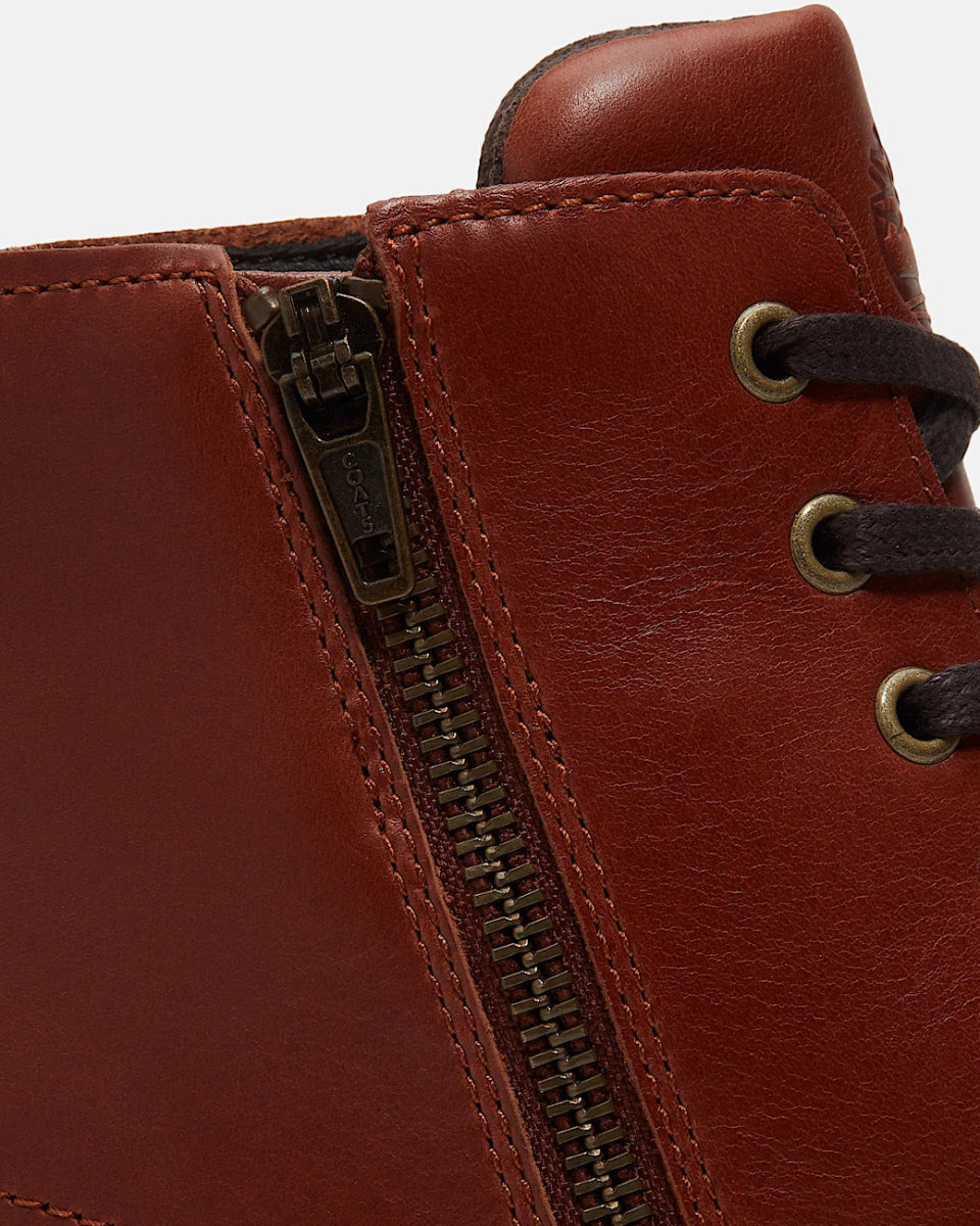 Close-up of a brown leather lace-up boot showing the side zipper and metal eyelets with dark brown laces against a light gray background.