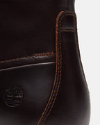 Close-up of a dark brown leather boot showing the side seam, contrast stitching, and an embossed Timberland tree logo on a light gray background.