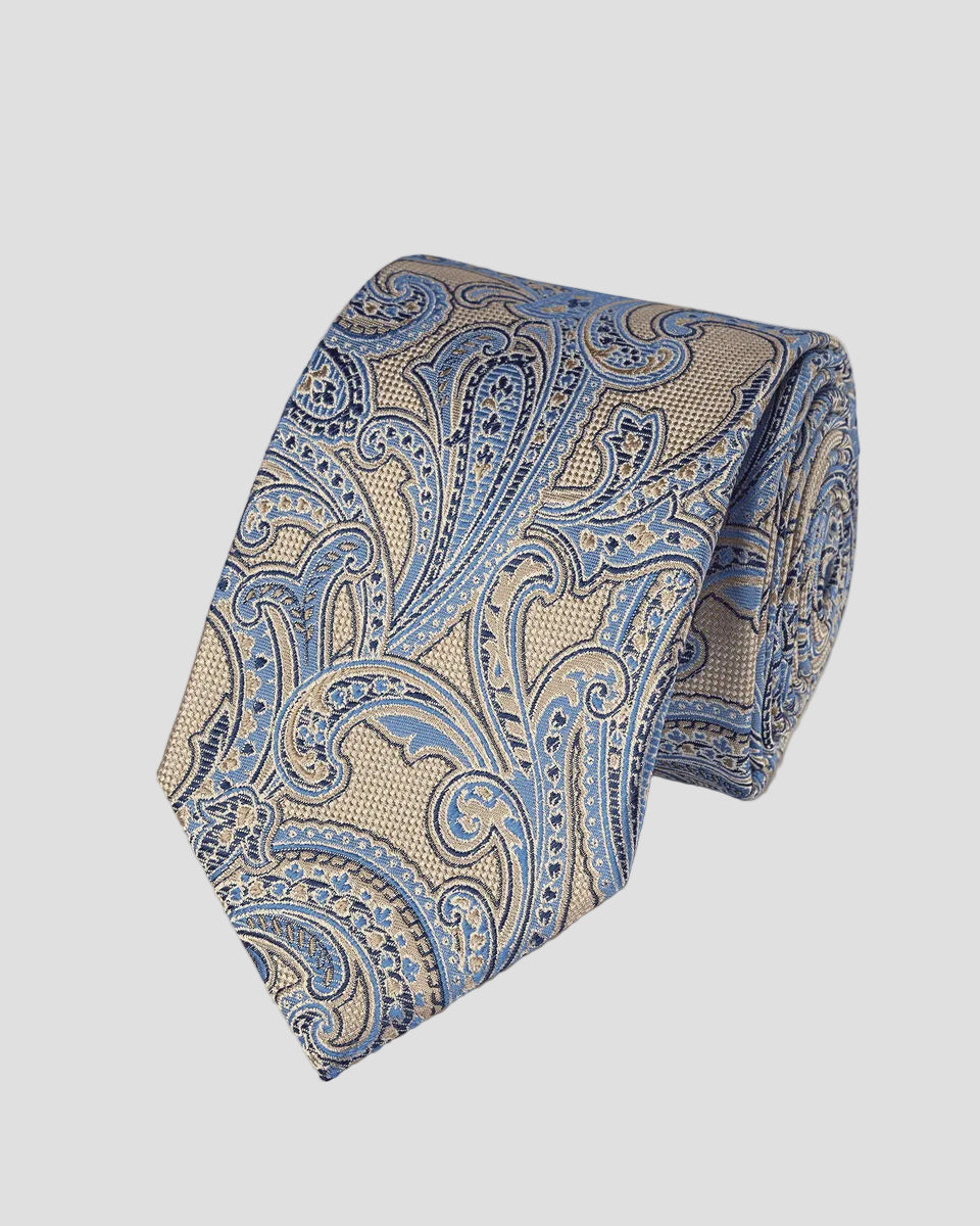 A rolled necktie featuring a detailed paisley pattern in shades of blue, beige, and gold, set against a solid light beige background.